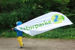 Ein kleines Kind schwenkt eine Fahne mit der Aufschrift Naturparke 24.